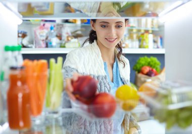 Sağlıklı yiyecek, sebze ve meyvelerle dolu açık buzdolabının yanında duran kadın portresi. Kadın portresi