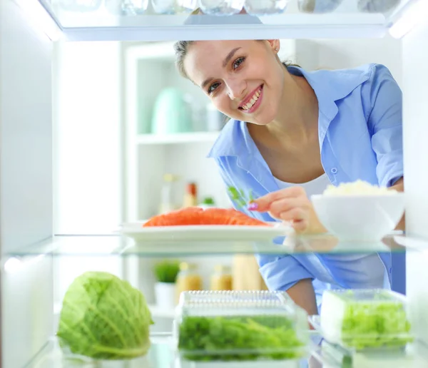 Portrait of female standing near open fridge full of healthy food, vegetables and fruits — Stock Photo, Image