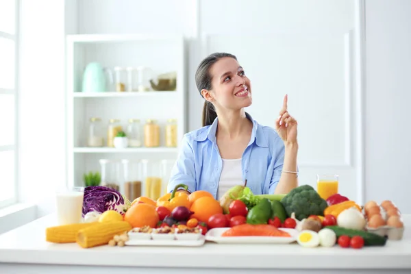 Young and cute woman sitting at the table full of fruits and vegetables in the wooden interior — Stock Photo, Image