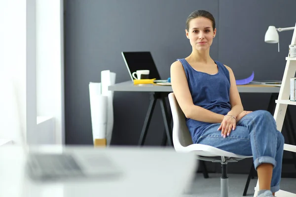 Ung kvinna sitter vid skrivbordet med instrument, plan och laptop — Stockfoto