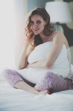 Yatağında otururken bir yastık tutan genç kadın.