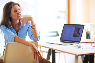 Ofis masasında dizüstü bilgisayarla oturan genç bir kadın. Genç bir kadın. Dizüstü bilgisayar