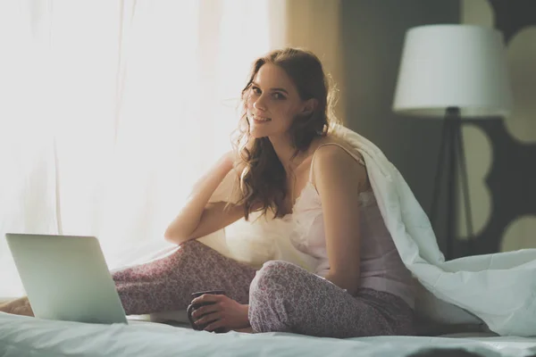 Dizüstü bilgisayar ile yatakta oturan genç güzel kadın. — Stok fotoğraf