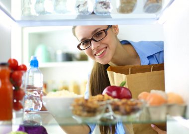 Sağlıklı yiyecek, sebze ve meyvelerle dolu açık buzdolabının yanında duran kadın portresi.
