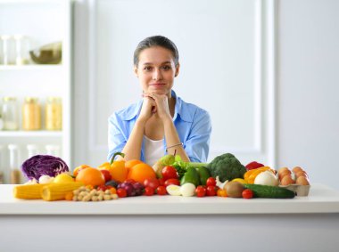 Ahşap iç kısımda meyve ve sebze dolu masada oturan genç ve tatlı bir kadın.