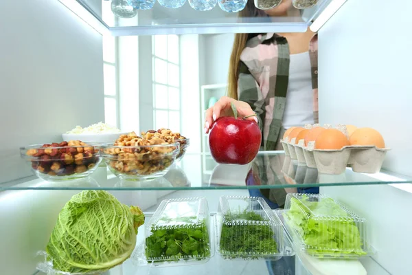 Portret kobiety stojącej w pobliżu otwartej lodówki pełnej zdrowej żywności, warzyw i owoców — Zdjęcie stockowe