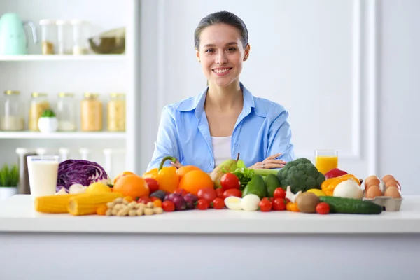 Jeune et mignonne femme assise à la table pleine de fruits et légumes à l'intérieur en bois — Photo