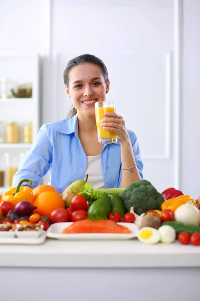 Young and cute woman sitting at the table full of fruits and vegetables in the wooden interior — Stock Photo, Image