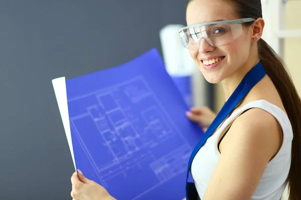 Jonge vrouw staande in de buurt van Bureau en kijken naar de blauwdruk van de nieuwe woning — Stockfoto