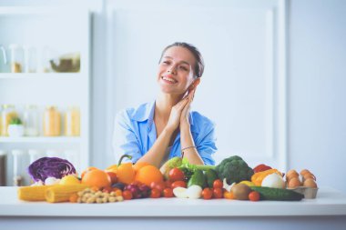 Ahşap iç kısımda meyve ve sebze dolu masada oturan genç ve tatlı bir kadın.