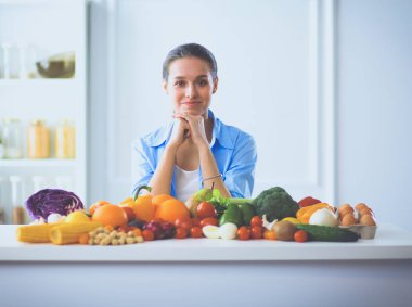 Ahşap iç kısımda meyve ve sebze dolu masada oturan genç ve tatlı bir kadın.