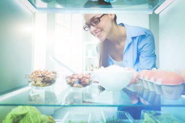 Sağlıklı yiyecek, sebze ve meyvelerle dolu açık buzdolabının yanında duran kadın portresi.