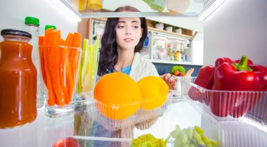 Sağlıklı yiyecek, sebze ve meyvelerle dolu açık buzdolabının yanında duran kadın portresi. Kadın portresi