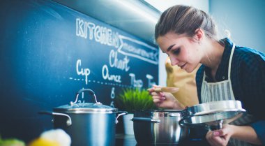 Mutfakta sobanın yanında duran genç bir kadın. .