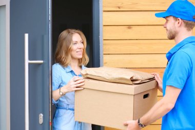 Mavi üniformalı gülümseyen kurye servis konseptine paket kutusu teslim eden teslimatçı. Mavi üniformalı gülümseyen teslimatçı.