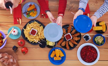 Ahşap masada otururken birlikte yemek yiyen bir grup insanın üst düzey görüntüsü. Masada yemek var. İnsanlar fast food yiyor..
