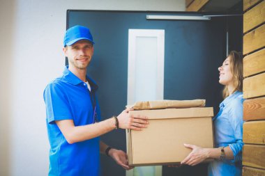 Mavi üniformalı gülümseyen kurye servis konseptine paket kutusu teslim eden teslimatçı. Mavi üniformalı gülümseyen teslimatçı.