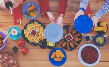 Ahşap masada otururken birlikte yemek yiyen bir grup insanın üst düzey görüntüsü. Masada yemek var. İnsanlar fast food yiyor..