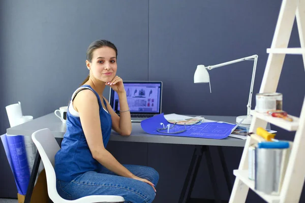 Ung kvinna sitter vid skrivbordet med instrument, plan och laptop — Stockfoto