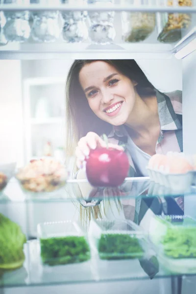 Portret van een vrouw in de buurt van een open koelkast vol gezond voedsel, groenten en fruit — Stockfoto