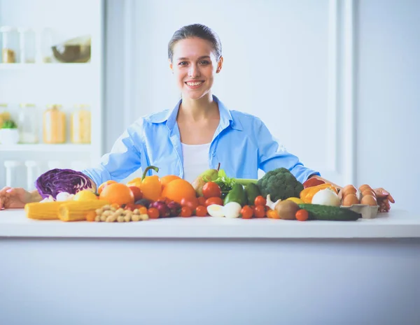 Mujer joven y linda sentada en la mesa llena de frutas y verduras en el interior de madera — Foto de Stock