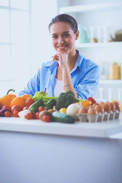 Femeia tânără și drăguță care stă la masă plină de fructe și legume în interiorul lemnului — Fotografie, imagine de stoc