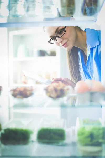 Retrato de fêmea em pé perto da geladeira aberta cheia de alimentos saudáveis, legumes e frutas — Fotografia de Stock