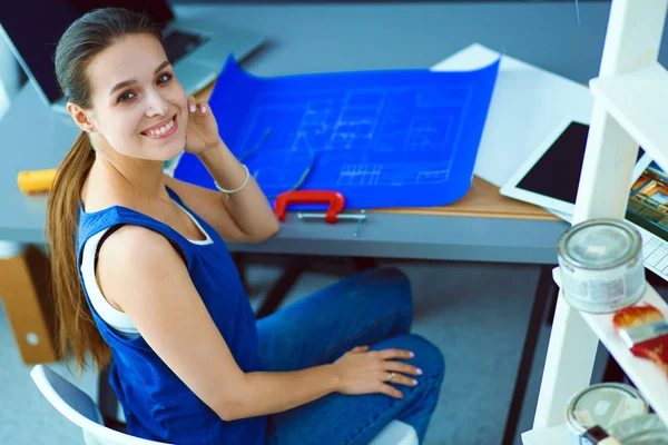 Young woman sitting at the desk with instruments, plan and laptop — Stock Photo, Image