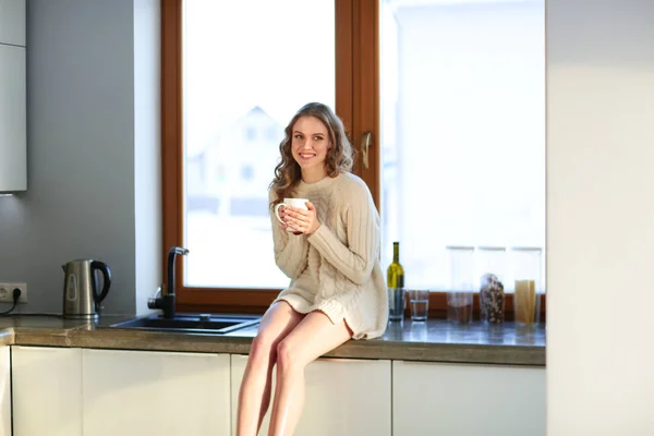 Portret van een vrouw met een kopje thee in haar keuken. — Stockfoto