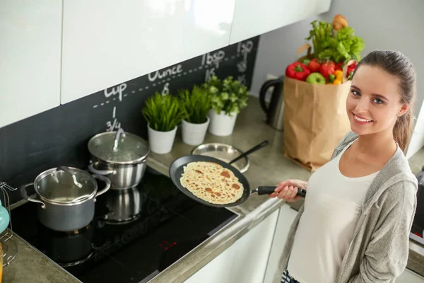 Mujer joven prepara panqueques en la cocina mientras está de pie cerca de la mesa. Mujer en la cocina. Cocinar en la cocina. —  Fotos de Stock