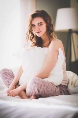 Yatağında otururken bir yastık tutan genç kadın.