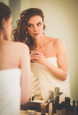 Genç bir kadın aynaya bakıyor ve makyaj yapıyor..