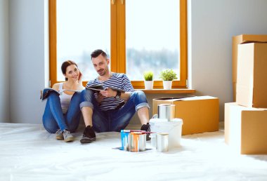 Yeni evin içini boyayan mutlu, gülümseyen genç bir çift portresi. Genç çift