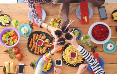 Ahşap masada otururken birlikte yemek yiyen bir grup insanın üst düzey görüntüsü. Masada yemek var. İnsanlar fast food yiyor..