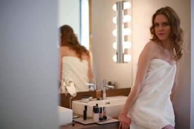 Genç bir kadın aynaya bakıyor ve makyaj yapıyor..