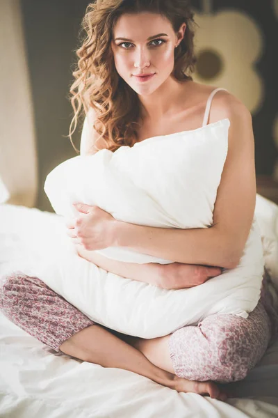Молода жінка тримає подушку, сидячи на ліжку . — стокове фото