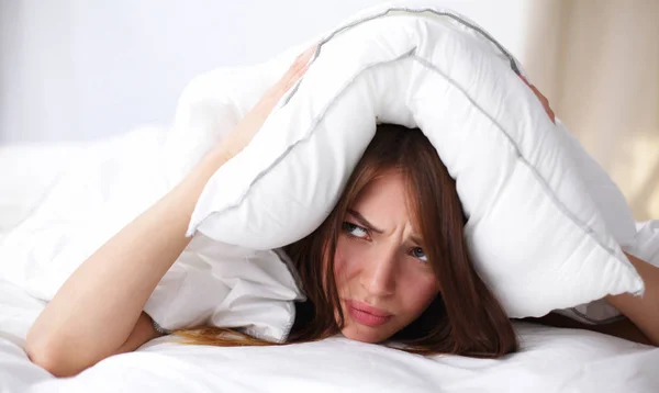 Kobieta leżąca na łóżku i zamykająca uszy poduszką — Zdjęcie stockowe