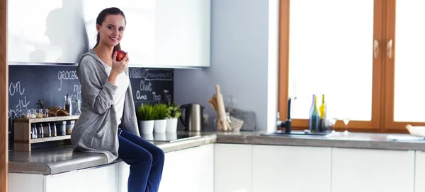 Mulher usando telefone celular sentado na cozinha moderna . — Fotografia de Stock