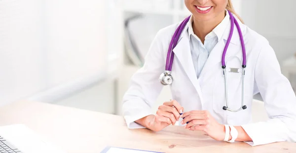 Mooie jonge glimlachende vrouwelijke arts zitten aan het bureau en schrijven. — Stockfoto