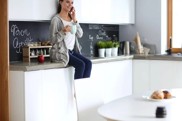 Mujer usando el teléfono móvil sentado en la cocina moderna . —  Fotos de Stock