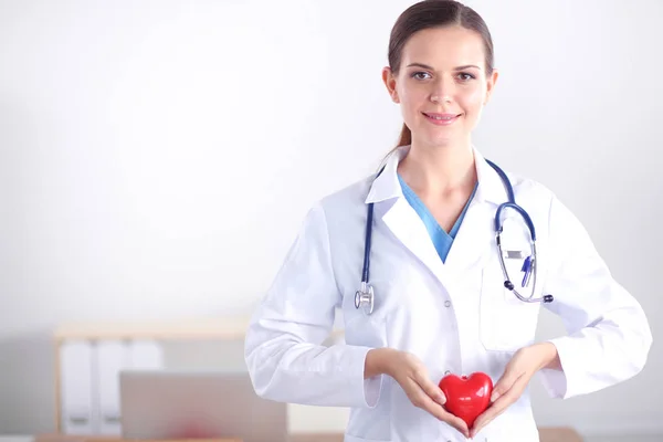 Masada oturan ve kalp tutan güzel genç gülümseyen kadın doktor. — Stok fotoğraf