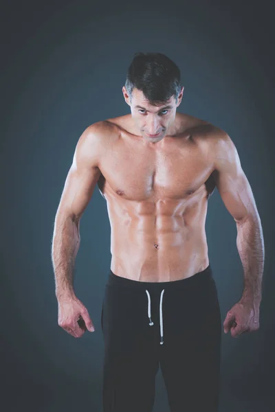 Svalnatý muž. Svalnatý muž na šedém pozadí ukazuje svaly. Fitness instruktor. Profesionální fitness. Cvičení. Pánské fitness. — Stock fotografie