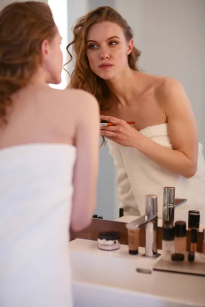Junge Frau schaut in den Spiegel und schminkt sich. — Stockfoto