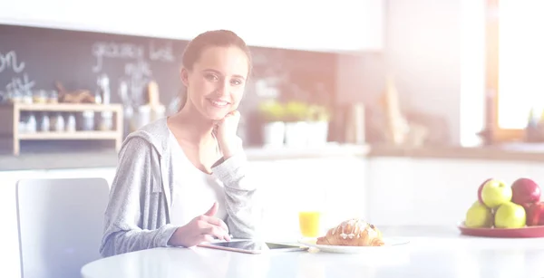 Młoda kobieta za pomocą cyfrowego tabletu w kuchni. Kobieta pije kawę i za pomocą cyfrowego tabletka rano. — Zdjęcie stockowe