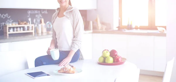 Jovem usando tablet digital na cozinha. Mulher bebendo café e usando tablet digital pela manhã . — Fotografia de Stock