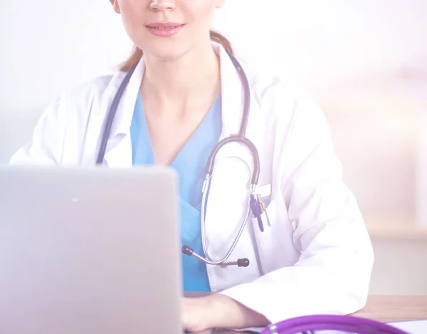 Médica trabalhando na mesa de escritório e sorrindo para a câmera, interior do escritório em segundo plano — Fotografia de Stock