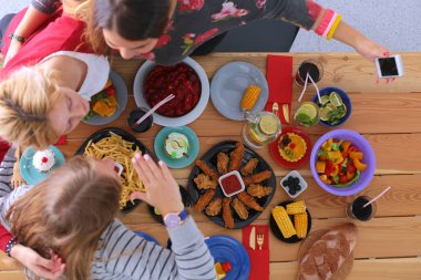 Ahşap masada otururken birlikte yemek yiyen bir grup insanın üst düzey görüntüsü. Masada yemek var. İnsanlar fast food yiyor..