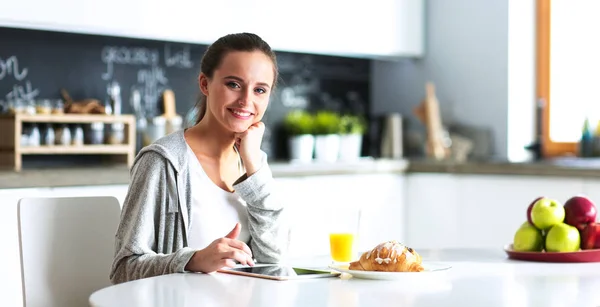 Mujer joven usando tableta digital en la cocina. Mujer tomando café y usando tableta digital en la mañana . —  Fotos de Stock