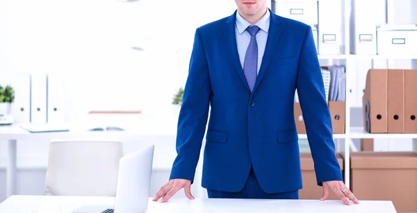 Glad affärsman stående på kontoret i bakgrunden fungerar genom skrivbordet — Stockfoto
