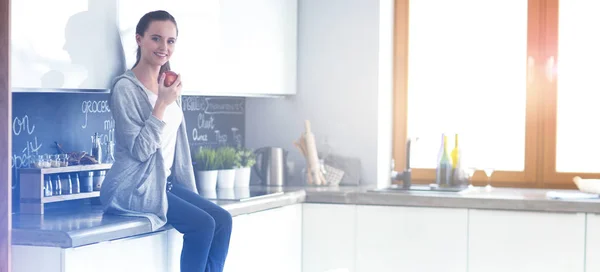 Mujer usando el teléfono móvil sentado en la cocina moderna . — Foto de Stock